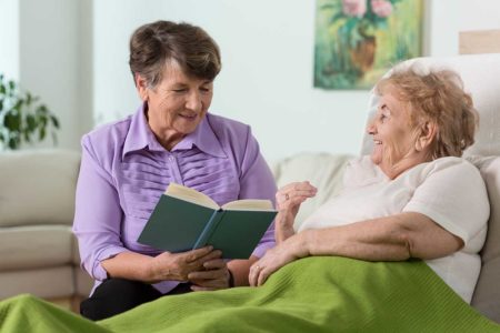 Hope Hospice's elderly volunteer is reading a book to another elderly woman