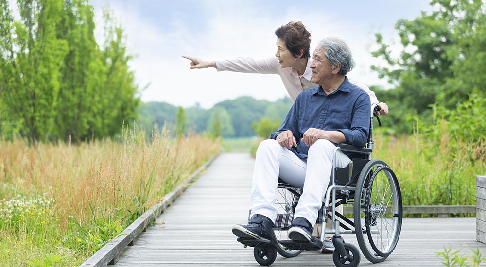 elderly asian man in wheelchair outdoors with wife