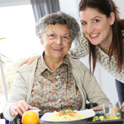 caregiver serving meal to elderly woman