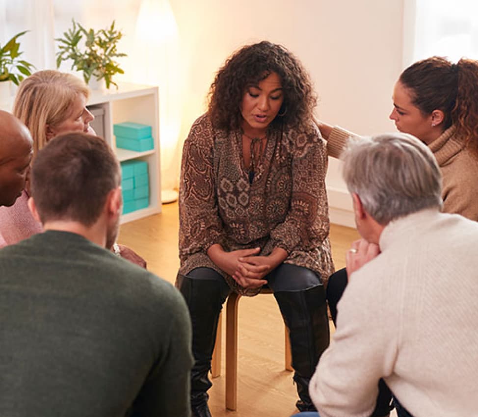 Woman sits surrounded by others, in a support group
