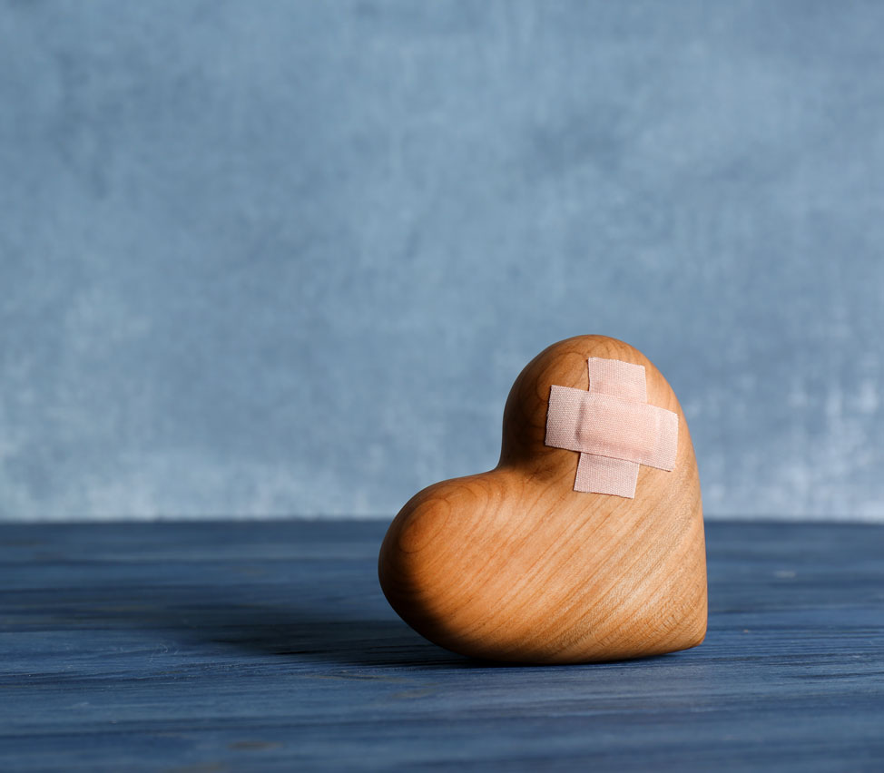 A small wooden heart with a two bandaids crossed on it.
